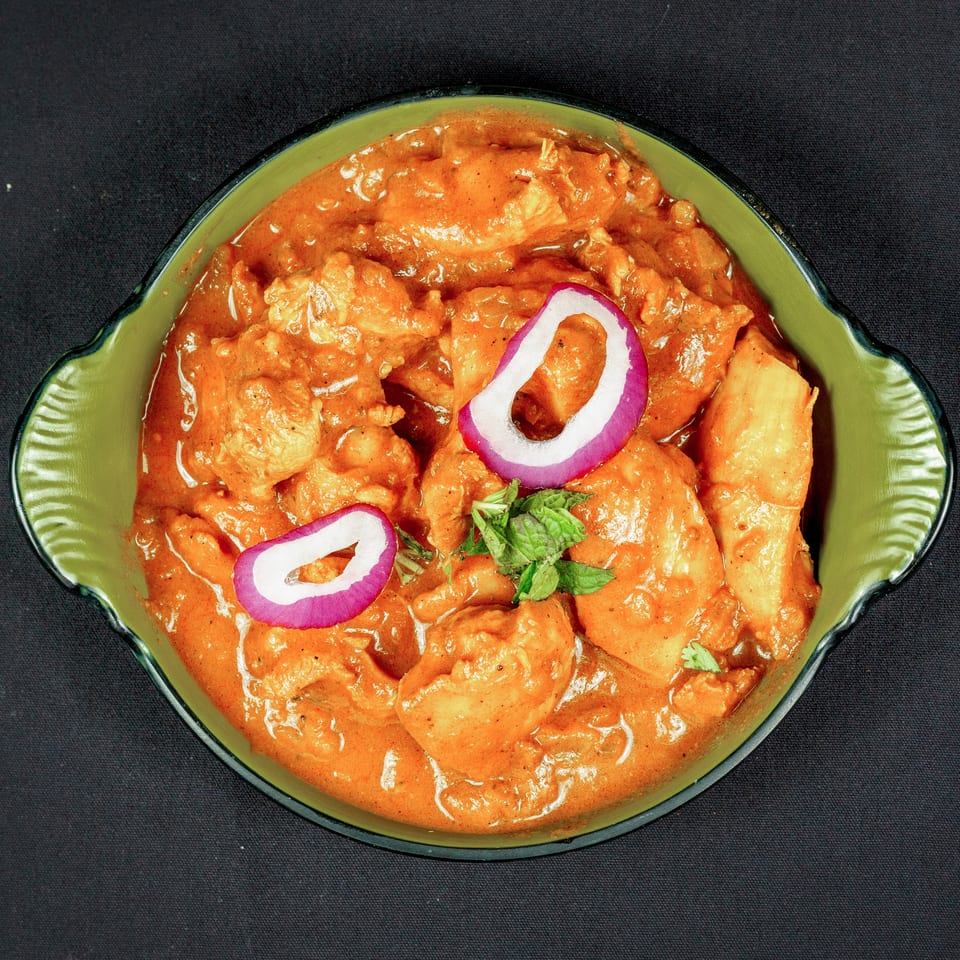 Creamy orange chicken curry garnished with red onion rings and fresh mint in a green bowl.