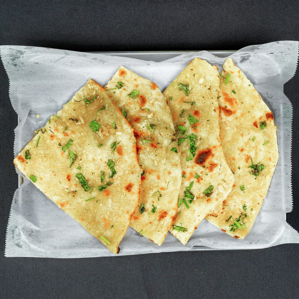 Several golden-brown garlic naan breads topped with cilantro, arranged on parchment paper.