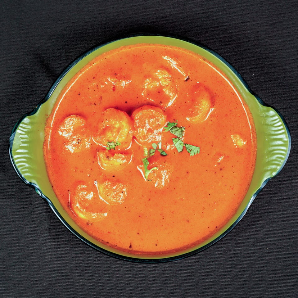 Creamy orange curry with shrimp and cilantro, served in a green dish against a black background.