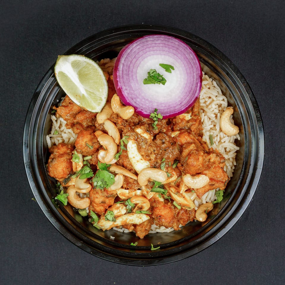 Indian curry with rice, cashews, cilantro, red onion, and lime served in a black bowl.