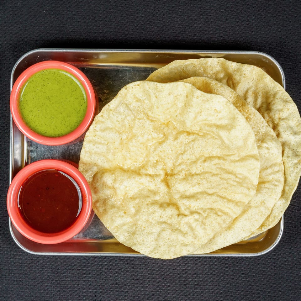 Golden fried puris served on a metal tray with green chutney and red dipping sauce.