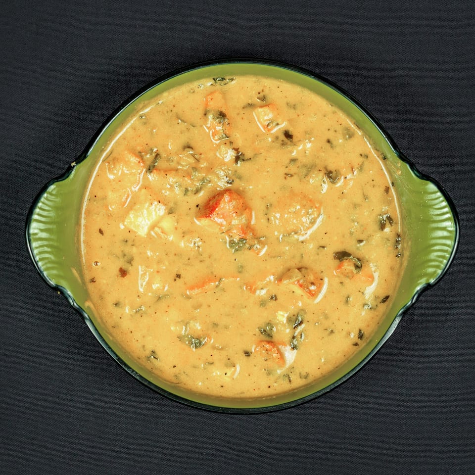 Creamy orange curry with shrimp and herbs served in a green scalloped bowl on black fabric.