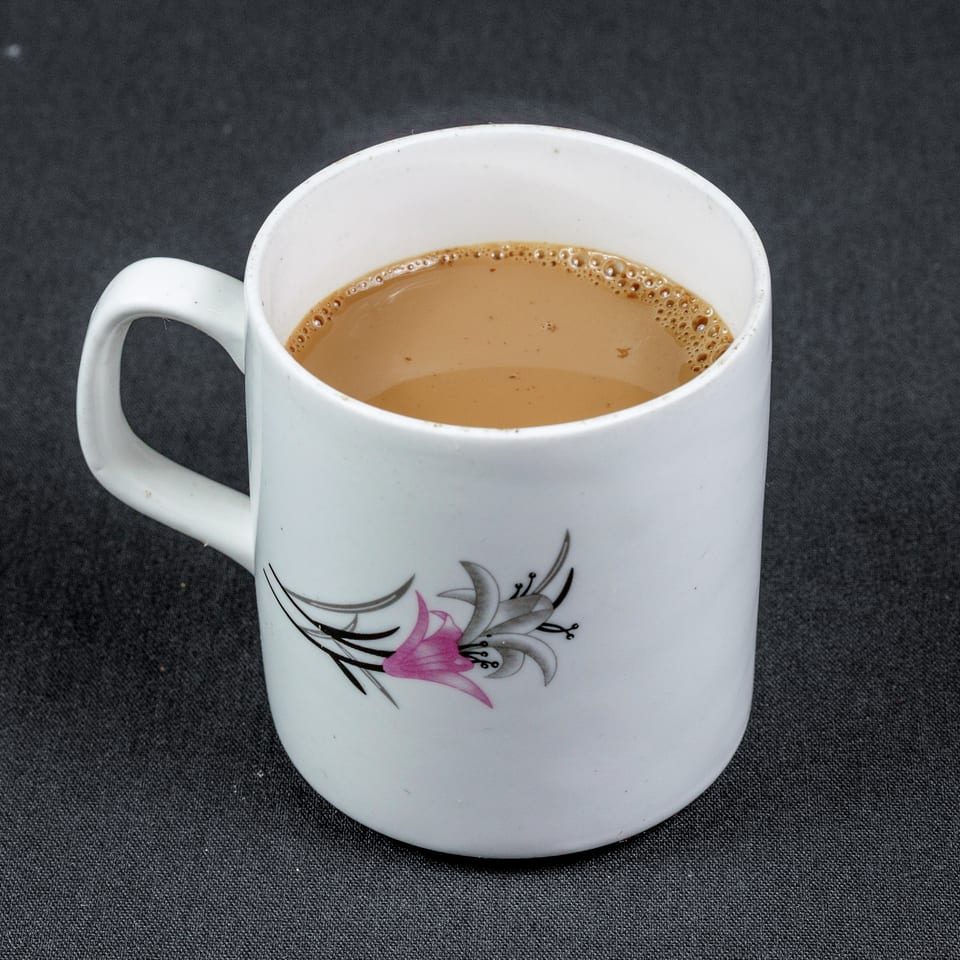 White floral mug filled with frothy tea on a dark textured surface.