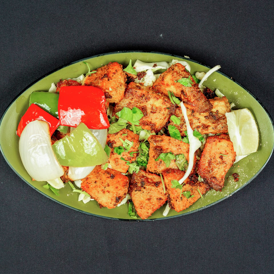 Grilled seasoned chicken pieces served with cabbage, bell peppers, onions, cilantro, and lime wedges on a green platter.
