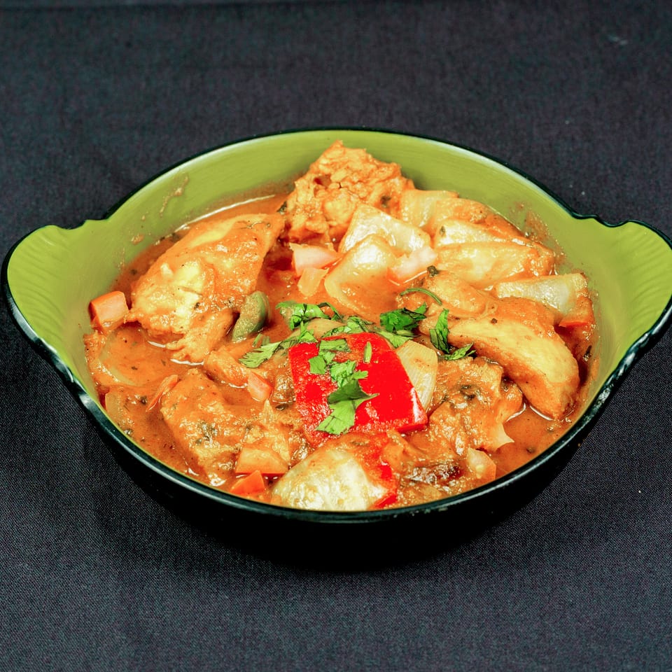 Bowl of creamy orange curry with chunks of protein, onions, peppers, and fresh cilantro garnish.