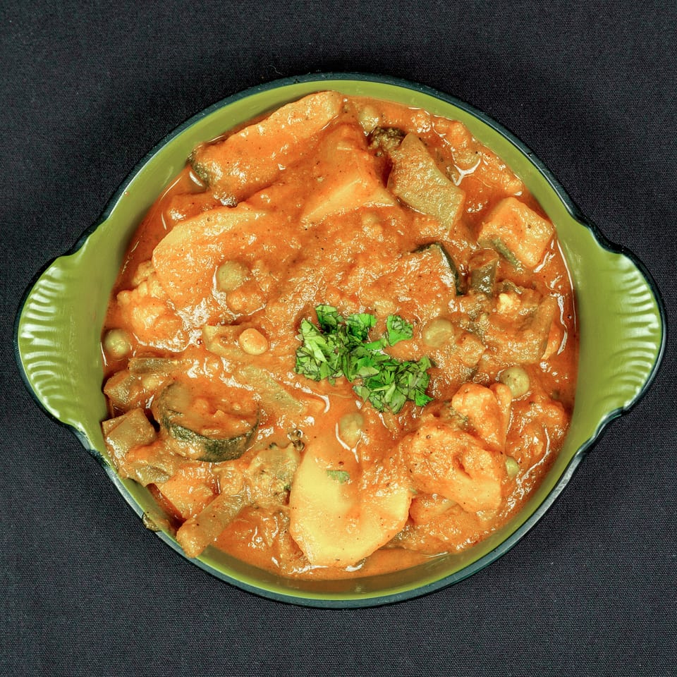 Creamy orange vegetable curry garnished with fresh cilantro, served in a green bowl on black fabric.