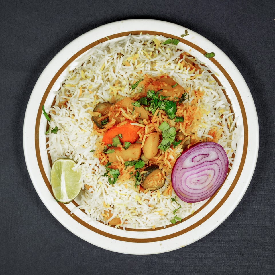 Overhead view of vegetable biryani with basmati rice, potatoes, carrots, cilantro, lime wedge, and red onion slices.