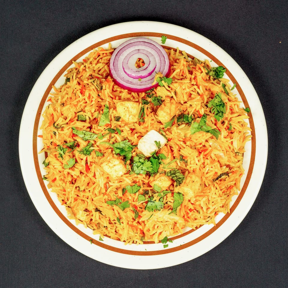 Plate of spiced biryani rice topped with chicken pieces, fresh cilantro, and red onion rings.
