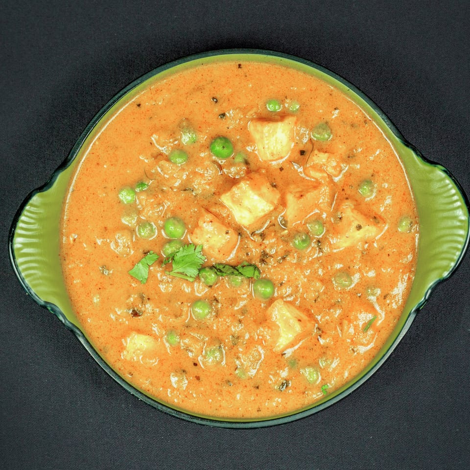 Creamy orange curry with paneer cubes, green peas, and cilantro served in a green bowl.