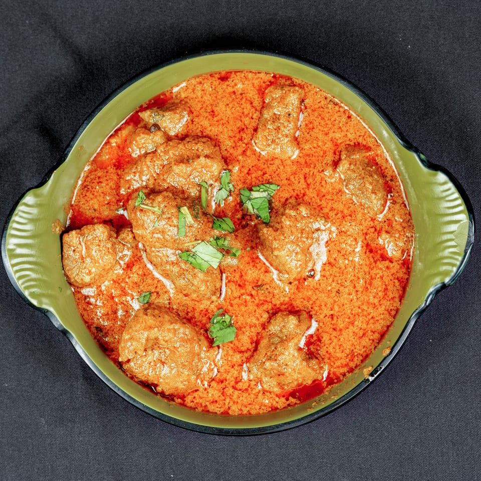 Bowl of meatballs in creamy red curry sauce, garnished with fresh cilantro.