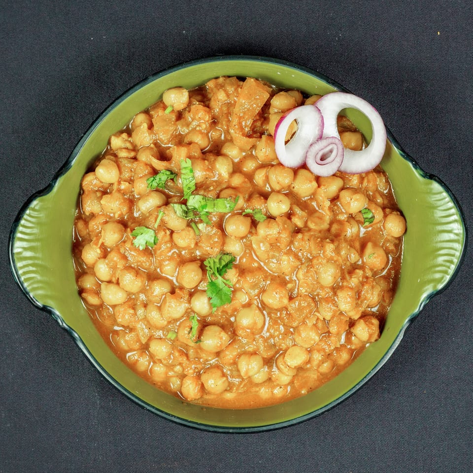 Bowl of chickpeas in orange curry garnished with cilantro and sliced red onion.