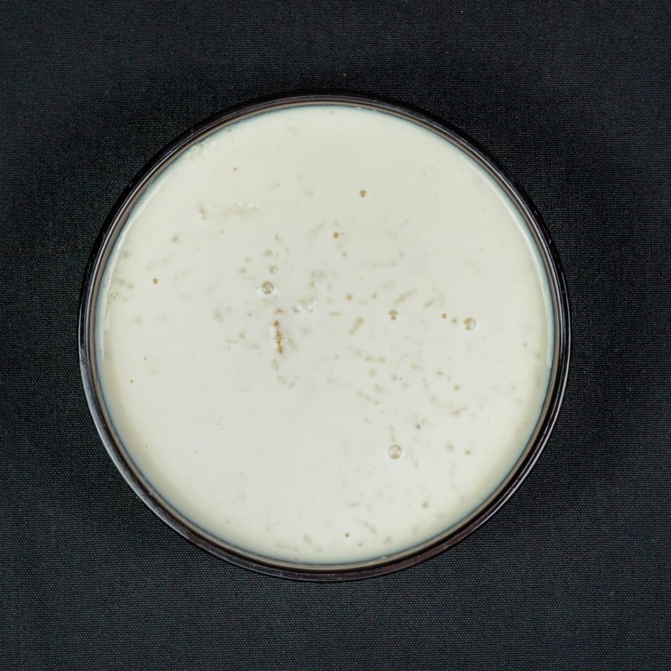 Overhead view of a glass bowl filled with creamy white soup or sauce on black textured fabric.